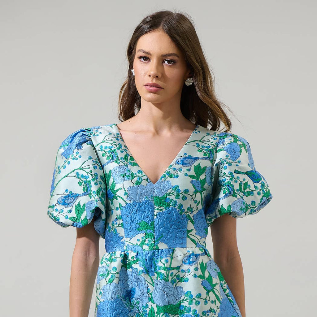 The bold floral pattern is sure to turn heads and brighten up any room you enter. This mini dress has textured jacquard style design with a v-neckline and puffy short sleeves. The open back has a tie string and zipper. Wear it with white strappy heels to complete the look.