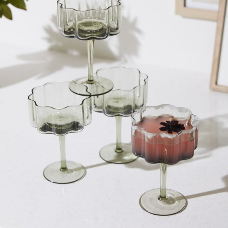 As decorative as it is functional, the Floret Coupe Glass is right at home styled on bar carts or open kitchen shelving. This trendy handmade solid glass drinkware elevates any cocktail party, event, or home bar with its smoky grey hue, scalloped rim, & vertical ridging. Food & dishwasher safe, this glass is even more beautiful arranged alongside the whole Floret glassware family.