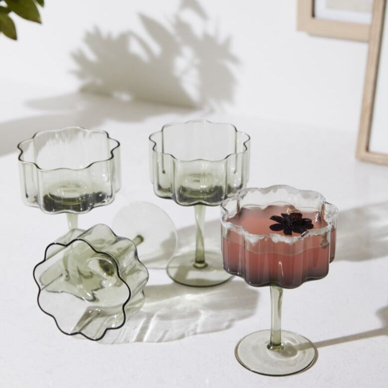 As decorative as it is functional, the Floret Coupe Glass is right at home styled on bar carts or open kitchen shelving. This trendy handmade solid glass drinkware elevates any cocktail party, event, or home bar with its smoky grey hue, scalloped rim, & vertical ridging. Food & dishwasher safe, this glass is even more beautiful arranged alongside the whole Floret glassware family.