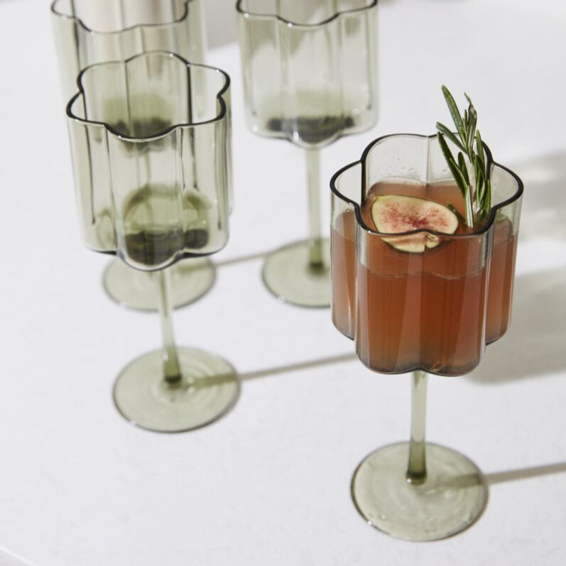 As decorative as it is functional, the stemmed Floret Wine Glass is right at home styled on bar carts or open kitchen shelving. This trendy handmade solid glass drinkware elevates any cocktail party, event, or home bar with its smoky grey hue, scalloped rim, &amp; vertical ridging. Food &amp; dishwasher safe, this glass is even more beautiful arranged alongside the whole Floret glassware family.