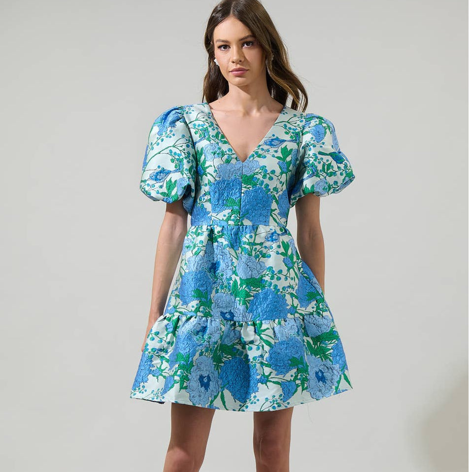 The bold floral pattern is sure to turn heads and brighten up any room you enter. This mini dress has textured jacquard style design with a v-neckline and puffy short sleeves. The open back has a tie string and zipper. Wear it with white strappy heels to complete the look.