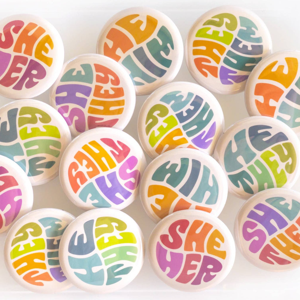 Wear your pronouns with pride with these cute retro-style buttons! This pinback button displays "She/They" pronouns in a vibrant color palette. It is the perfect way to let others know how to address you and to show your support for the LGBTQ+ community!  Size: 1.25" pinback button