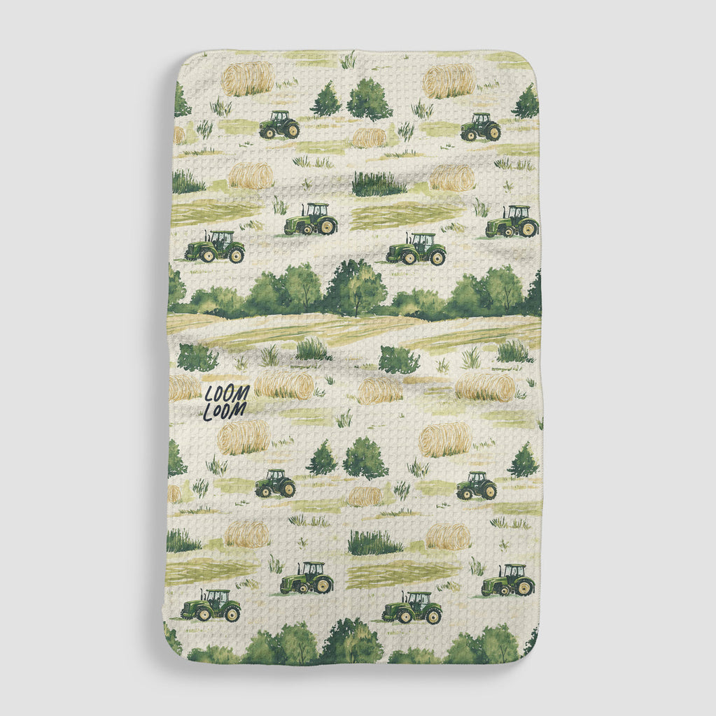 cream tea towel covered in farmland featuring hay and green tractors