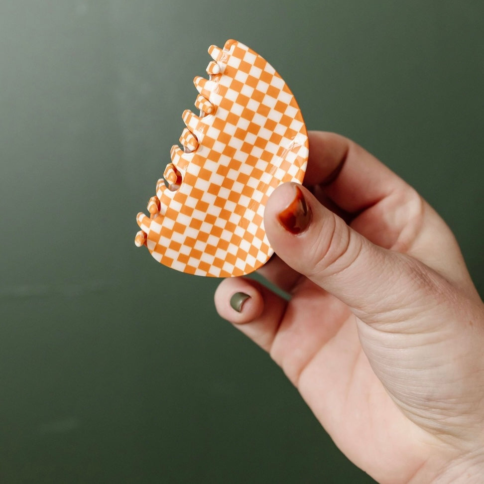 Put a playful spin on your hair with our Orange Checkered Claw Clip! Its classic design and chunky size make it the perfect retro accessory for any hairdo. Say goodbye to boring hair days and hello to a touch of fun and flair!