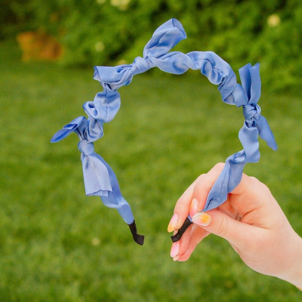 This sleek headband is made from soft, silky fabric in a charming blue color. With delicate bow accents, it's the perfect addition to any outfit. This headband is both comfortable and stylish! Give your hair a little something extra with this precious accessory.