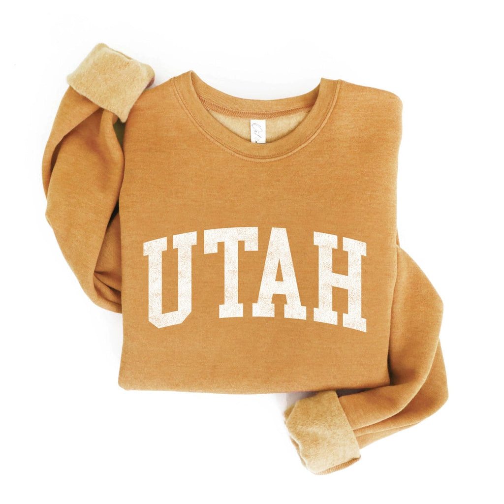 Get the "must-have" look with our Utah Graphic Sweatshirt! This soft, sponge fleece fabric in a trendy heather mustard color is the perfect unisex pullover. The ribbed cuffs and waistband add a touch of style to this crewneck, featuring "Utah" in eye-catching font. This is perfect for your next ski trip, throwing over your hiking clothes or strolling the streets of Salt Lake City.