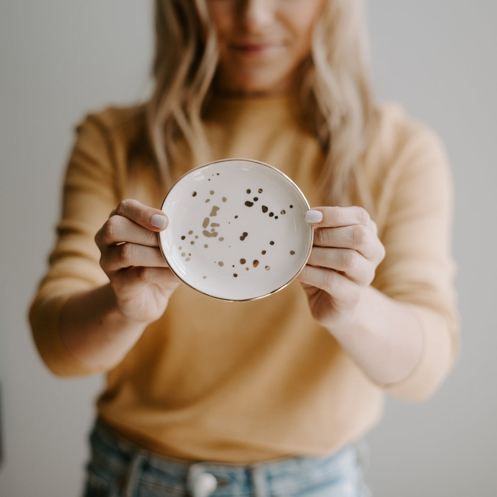 Organize jewelry in style with our White Gold Speckled Jewelry Dish. This beautiful white trinket tray is the perfect addition to any room. The gold foil details add a touch of chic glam, making it easy to dress up any space!