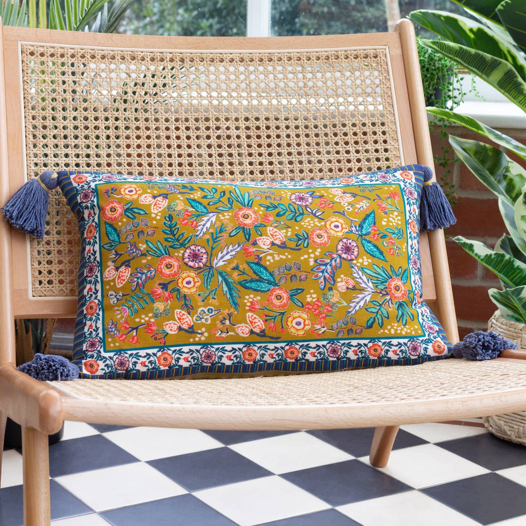 In a vivid, unique design, this cushion is adorned with vibrantly printed florals which are scattered liberally around the front and set on a deep ochre background. The design is surrounded by an intricate floral border, with a deep navy and yellow patterning around the edge, all printed on soft cotton. Finished with a chunky tassel trim, this design will layer well within a modern country interior.