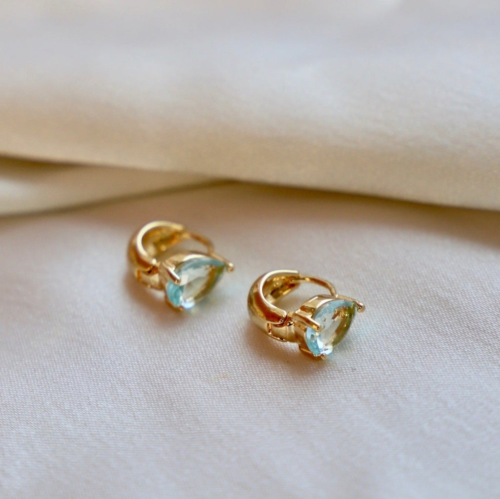 These elegant Crystal Teardrop Huggies feature a beautiful crystal aquamarine cz teardrop on a gold huggie earring. The combination of classic gold and sparkling crystal creates an eye-catching piece for any occasion.