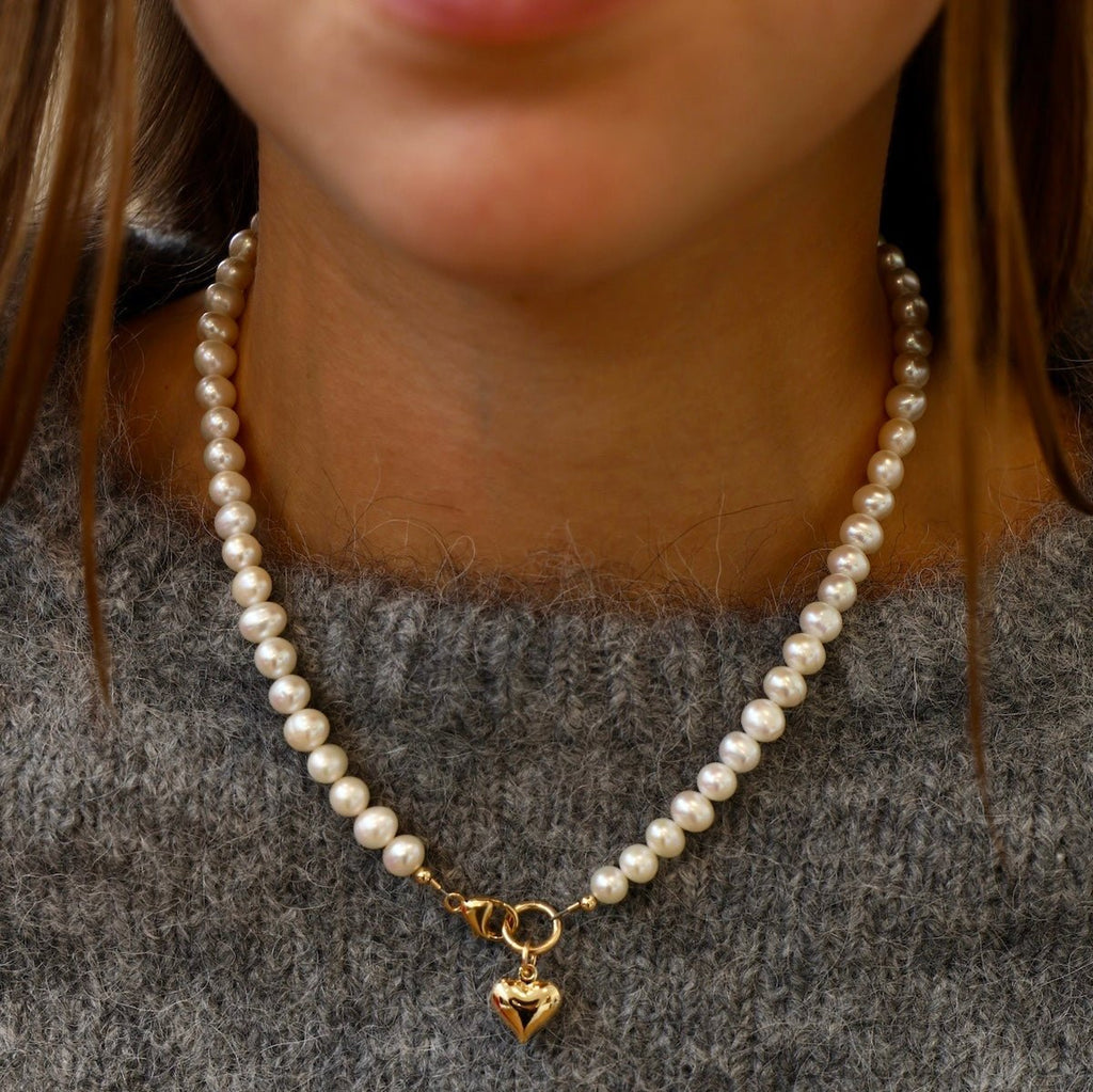 A freshwater pearl necklace with a front clasp with a gold puff heart. 