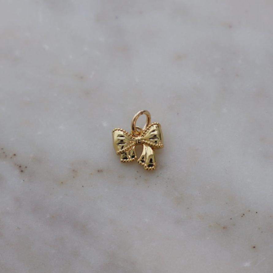 Add a touch of whimsy to your style with our Golden Bow Charm. This playful accessory is the perfect addition to any outfit, adding a touch of charm and fun. Made with a shiny golden material, this bow charm is sure to catch the eye and bring a smile to your face