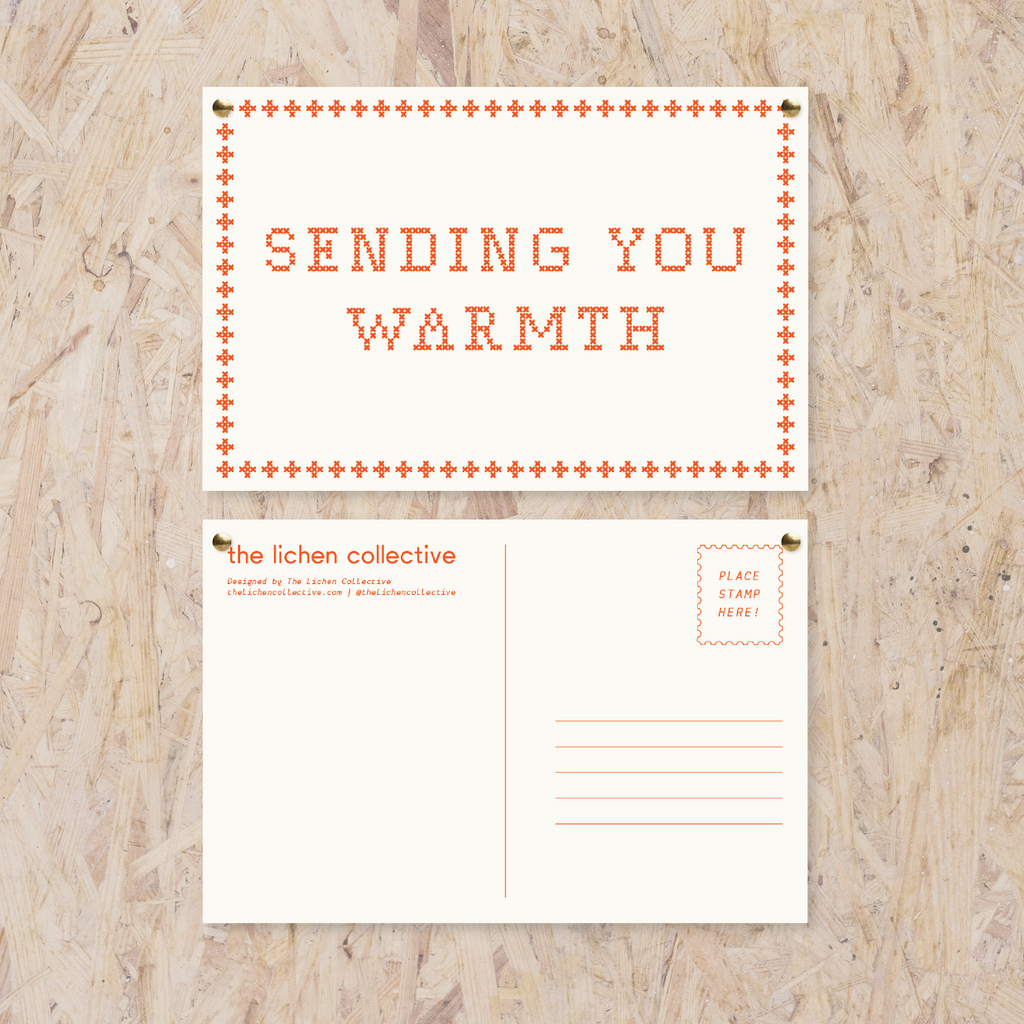 white postcard reading "sending you warmth" in a red cross stitch-like font