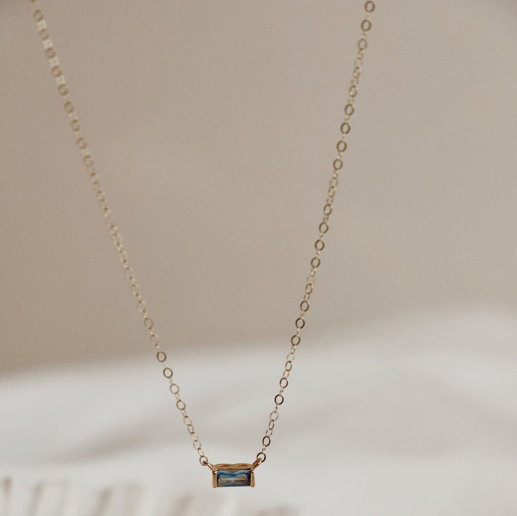 The necklace features a mesmerizing floating aqua cz baguette charm, adding a unique shimmer to any stack. It offers a timeless piece that will elevate your style on it's own or layered with our other chains.