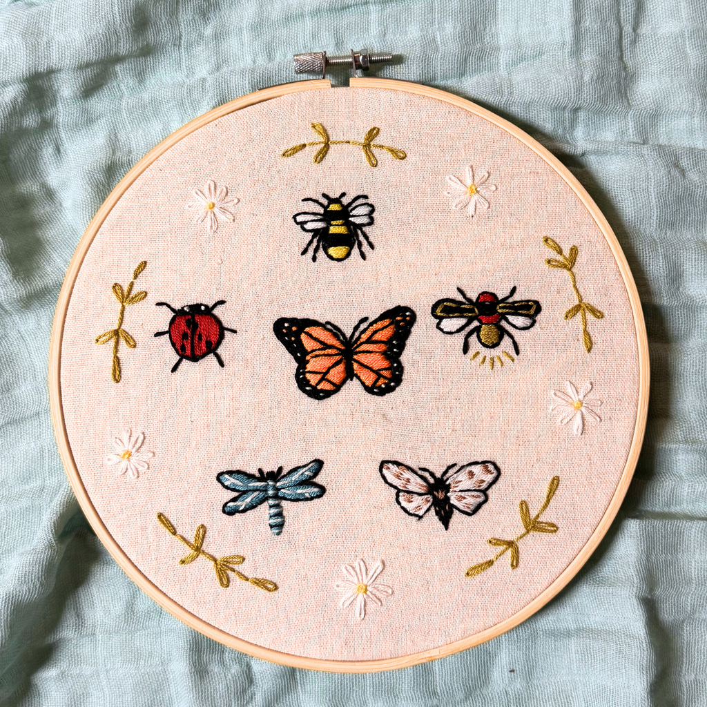 8 inch embroidery hoop featuring a wide variety of bugs (bumble bee, ladybug, dragonfly, beetle, butterfly, and moth) surrounded by flowers and greenery 