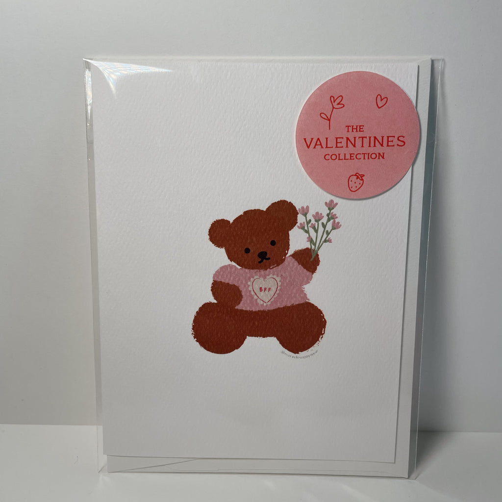 white valentine's day card featuring a teddy bear holding a bouquet of pink flowers and wearing a pink shirt that reads "BFF"