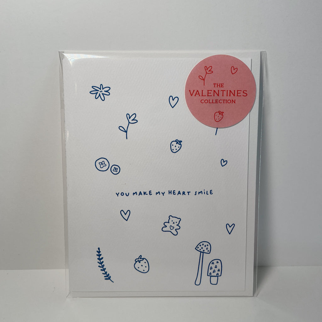 white valentine's card featuring blue doodles of flowers, hearts, berries, mushrooms, and  teddy bear