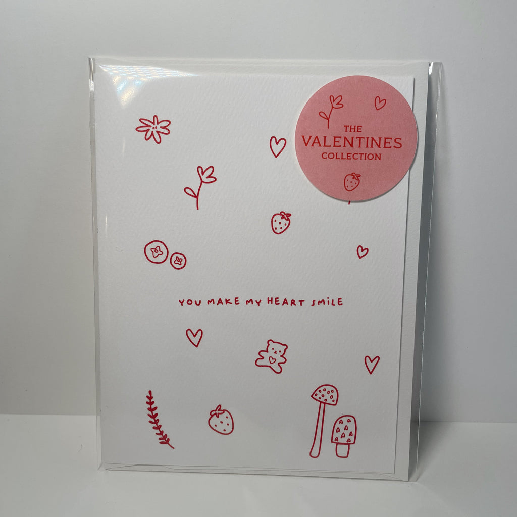 white valentine's card featuring red doodles of flowers, hearts, berries, mushrooms, and  teddy bear