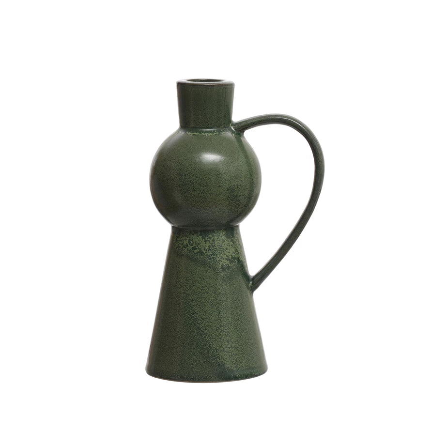 Illuminate the home with this green stoneware taper holder with a handle. This candle holder features a stoneware construction that has a reactive glaze that creates a beautiful variation of green hues. The candle holder has a unique shape that resembles a jug with a handle, adding some personality and flair to any space.