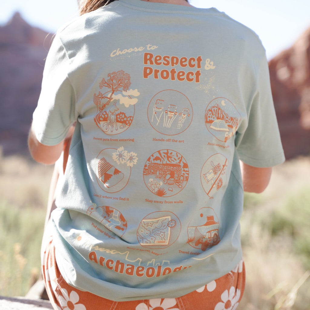 Blue and orange tee shirt. A pottery sherd decorates the front left chest. A dreamy how-to graphic with postcard feels adorns the back. Other hand-drawn highlights include a starry butterfly and Canyonlands National Park pictograph.