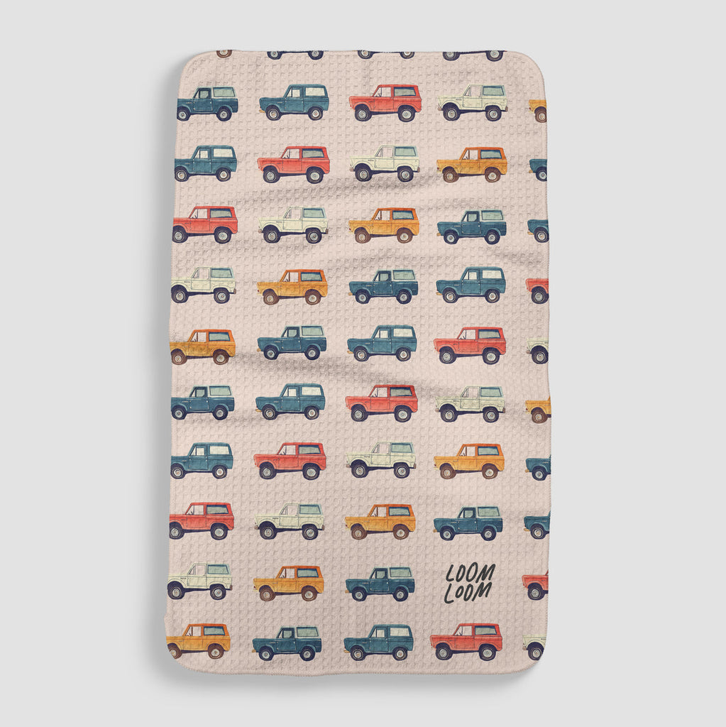 baby pink tea towel with rows of vintage broncos in blue, yellow, red, and white