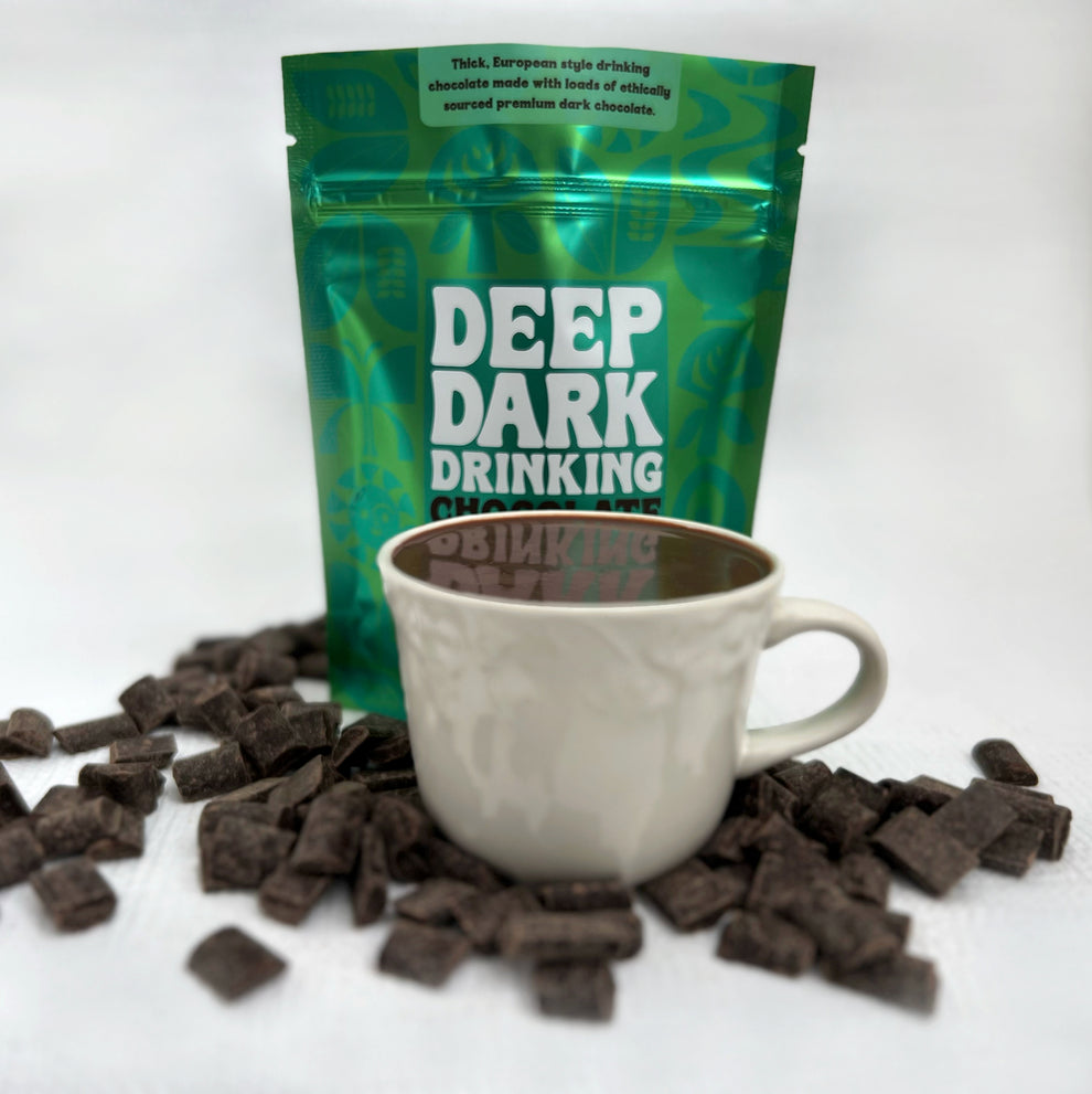 green bag of deep dark drinking chocolate daily fix with a cup of drinking chocolate and chocolate shavings