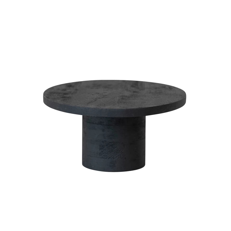 This black mango wood pedestal is a wonderful way to add height and elegance to the home. The pedestal is made of mango wood painted black and polished to create a smooth, shiny surface. The pedestal has an oval shape ideal for elevating or displaying cakes, pies, or other desserts that suit any farmhouse, French country, lodge, or Scandinavian home.