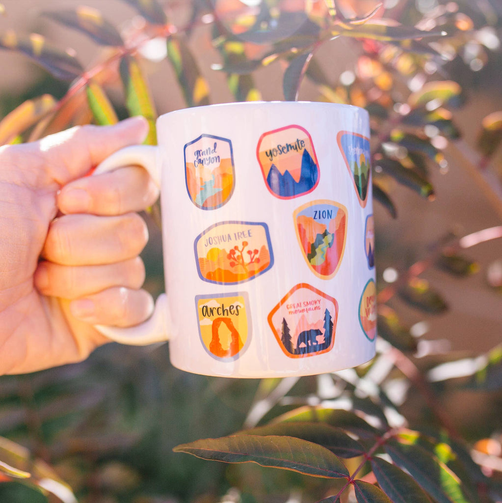 Embark on a sip-worthy journey with our National Parks Postage Stamps Mug. Perfect for coffee, tea, or sparkling water, this drinkware is an excellent gift for nature lovers, travel enthusiasts, and fans of America's national treasures. This cup features hand-drawn postage-style icons of parks including Olympic, Grand Teton, Glacier, Redwoods, Denali, Joshua Tree, Bryce Canyon, Grand Canyon, Yellowstone, Rocky Mountain, Everglades, Badlands, Hawaii Volcanoes, Big Bend, Great Smoky Mountain, Acadia and more!