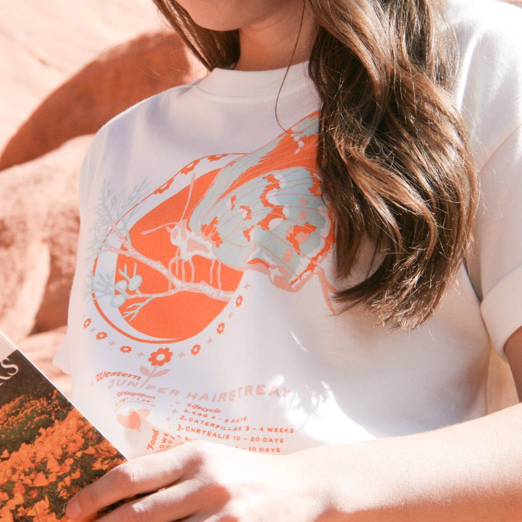 white tee shirt featuring an orange, pink, and blue butterfly on a branch along with the butterfly lifecycle