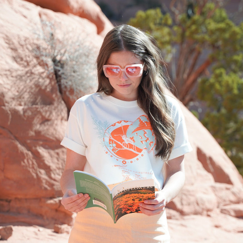 white tee shirt featuring an orange, pink, and blue butterfly on a branch along with the butterfly lifecycle