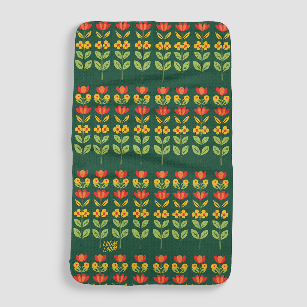 dark green tea towel featuring Swedish inspired flowers in different shades of yellow, orange, and red