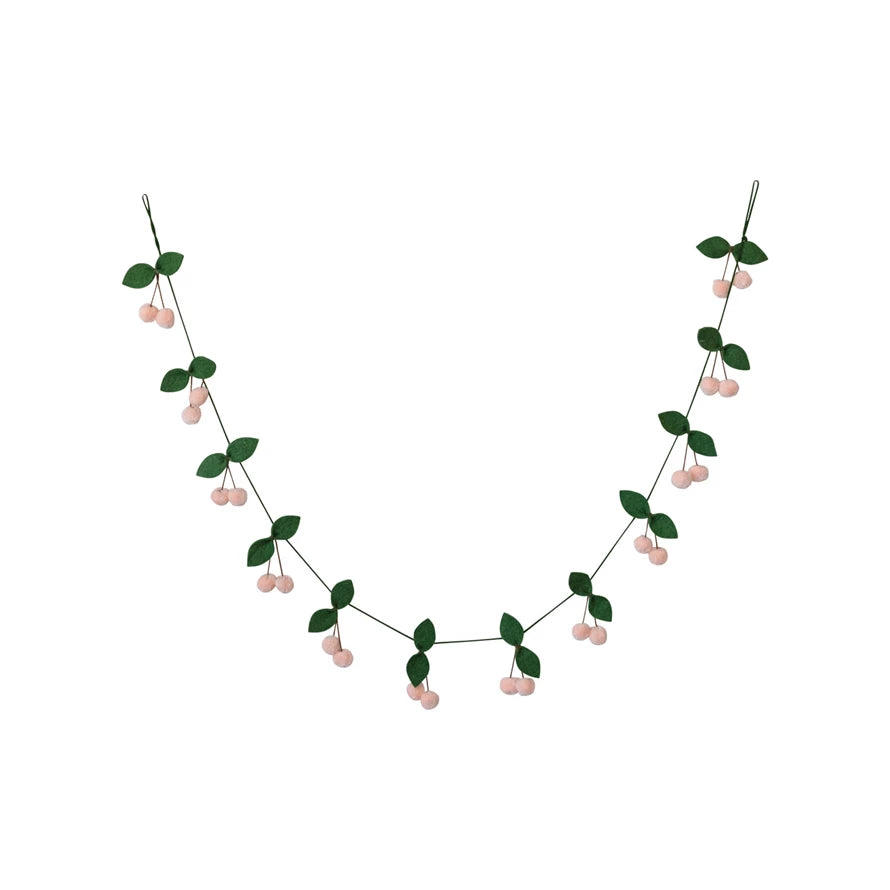 This handmade wool felt leaves and pom pom cherries garland is a whimsical creation that captures the essence of a verdant orchard. Crafted with care, each leaf and cherry pom pom is made from multicolored wool, creating a playful contrast of green, pink, and brown.