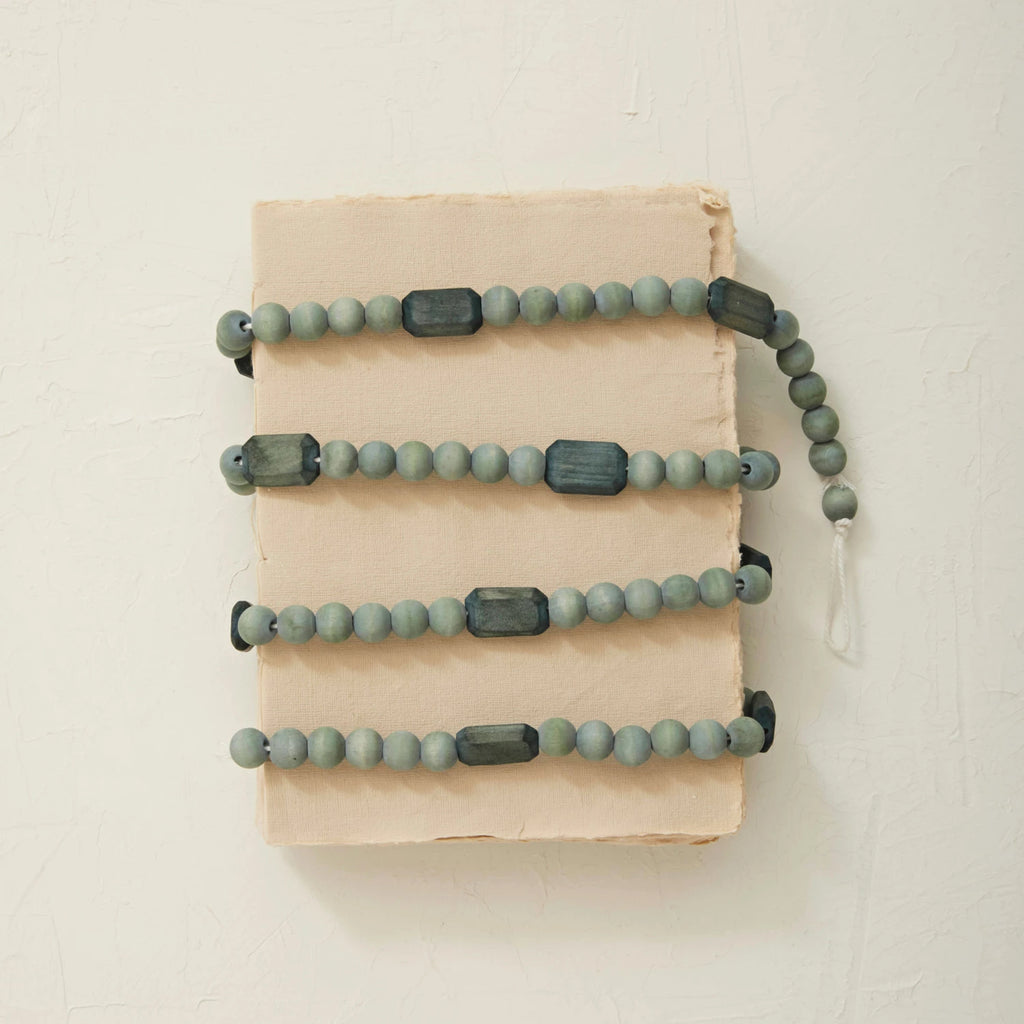 This paulownia wood bead garland in grey is a celebration of traditional holiday colors. Each bead is carefully crafted from Paulownia wood, known for its lightness and durability, and adorned with a natural finish that complements the vibrant grey hue. The garland's length of 72 inches and height of 0.75 inches make it a versatile choice for any festive display. Whether it's part of the Christmas decor or a year-round accent, this garland brings a touch of eco-friendly elegance and seasonal joy to the home